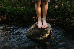 Person standing on stone in river in barefeet