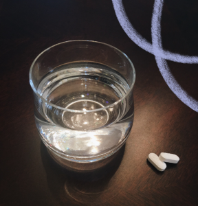 a clear glass of water is placed next to two white medication tablets on a brown table