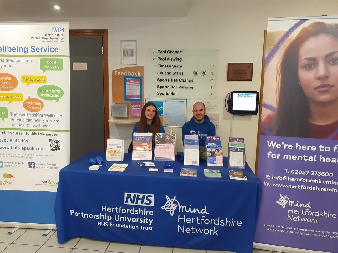 the photo shows our staff members Ciara and James sitting behind a promotional stall and smiling straight at the camera