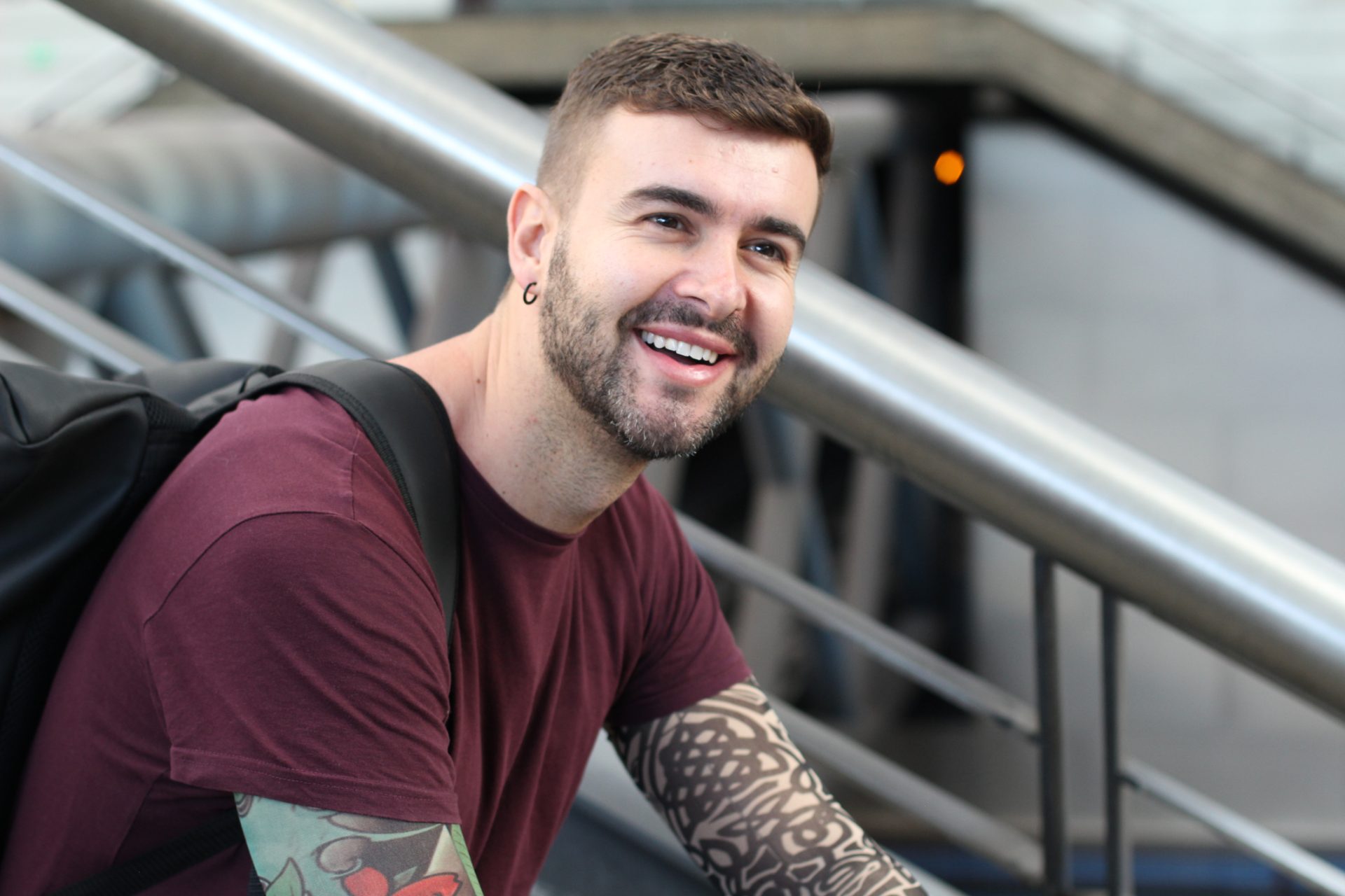 A smiling young man with a back pack, sat on steps