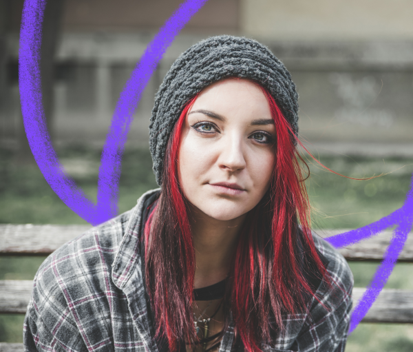 a young white girl with long red hair is staring at the camera with a neutral expression, she is wearing a wolly hat on her head and a stripy shirt.