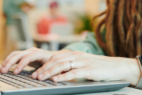 A young woman with dreadlocks, typing on her laptop.