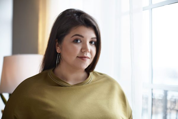 a white women with long dark hair is looking at the camera with a neutral expression, she is wearing a light green jumper