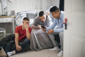 Three teenage boys looking at their mobile phones and chatting.