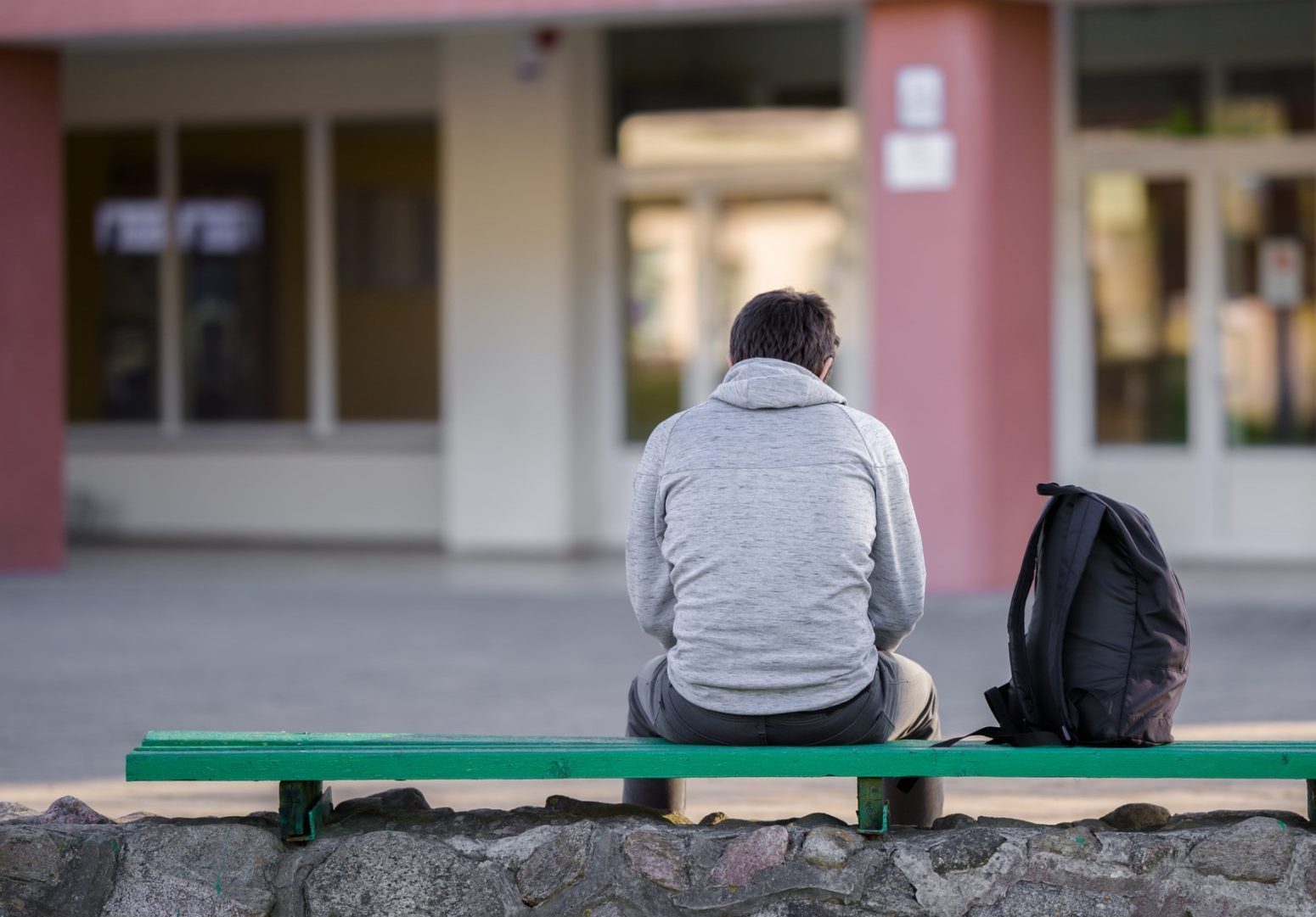 The back of a man sat on a bench outside